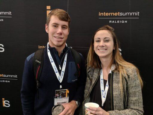two students with conference passes on lanyards around their necks stand in front of a black background.